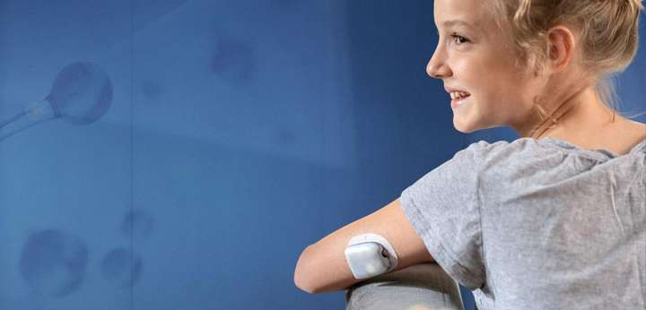 Child sitting on a chair smiling with on-body deliver system attached to arm.