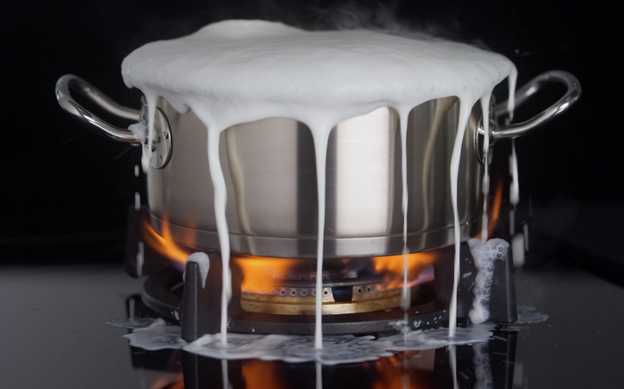 Cooking pot overflowing with milk on glass hob top