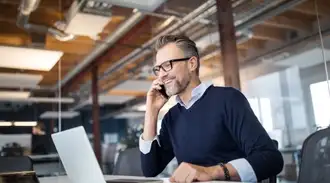 Man in glasses in business office on phone while working on laptop