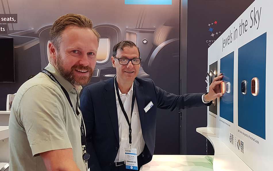 Ben Rowan and Philip Fischer touching the Jade Reading Light displayed at the SCHOTT booth at  Aircraft Interiors Expo 2022