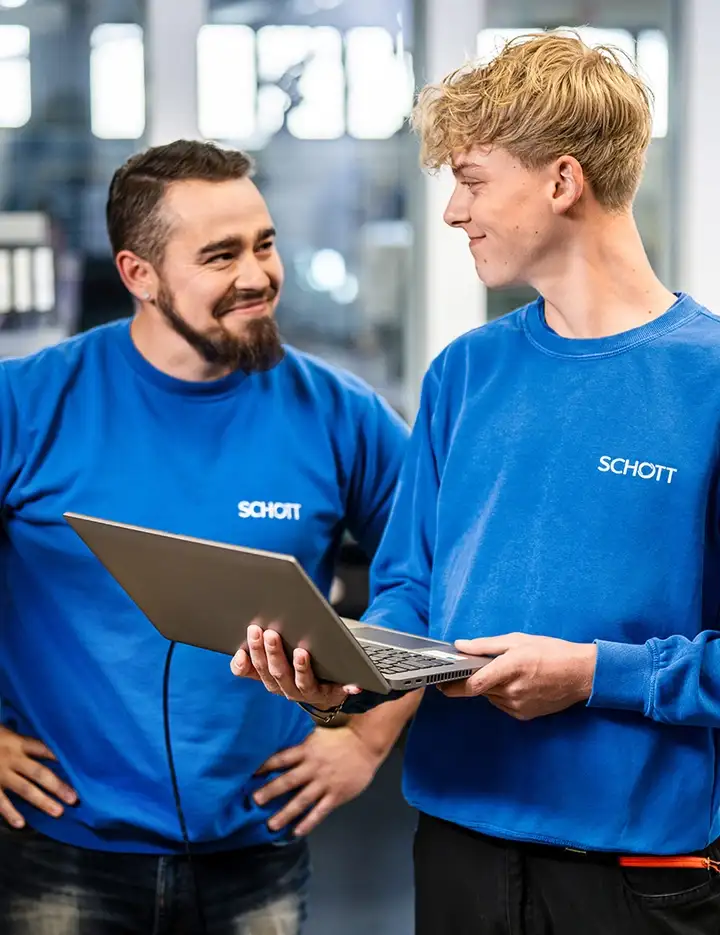 Zwei männliche Personen in blauen SCHOTT Pullovern stehen sich in einer Werkstatt gegenüber