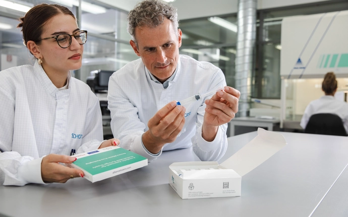 Frau und Mann im Reinraum, in Laborkleidung entnehmen Spritzen aus der Verpackung und begutachten diese.