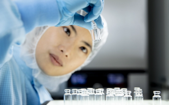 Frau in Reinraumkleidung prüft ein Pharmafläschchen.