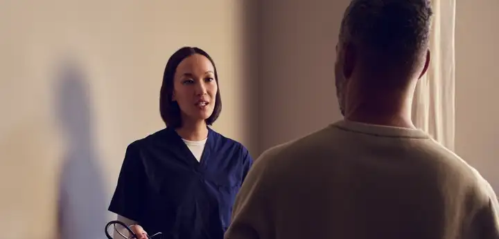 Healthcare worker in blue scrubs speaking with a patient indoors