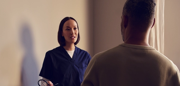 Healthcare worker in blue scrubs speaking with a patient indoors