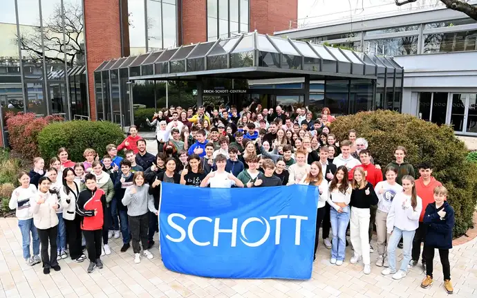 Teilnehmende Mädchen und Jungen am Wettbewerb Mathematik ohne Grenzen vor dem Erich-Schott-Centrum in Mainz mit SCHOTT Flagge