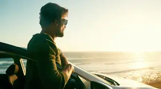 A person in sunglasses stands beside a car and looks out at the ocean.