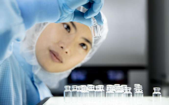 Woman in cleanroom suit checks a pharmaceutical vial