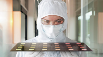 A woman in cleanroom clothing carries a tray  with several chips