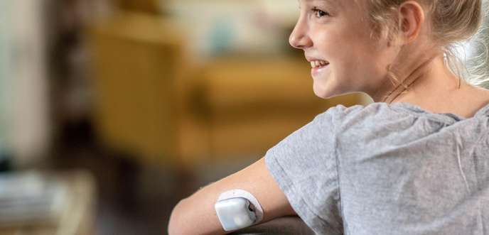 Child sitting on a chair smiling with on-body deliver system attached to arm.