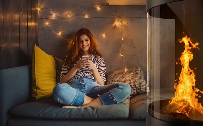 Woman sitting with her smartphone on a sofa beside a fireplace