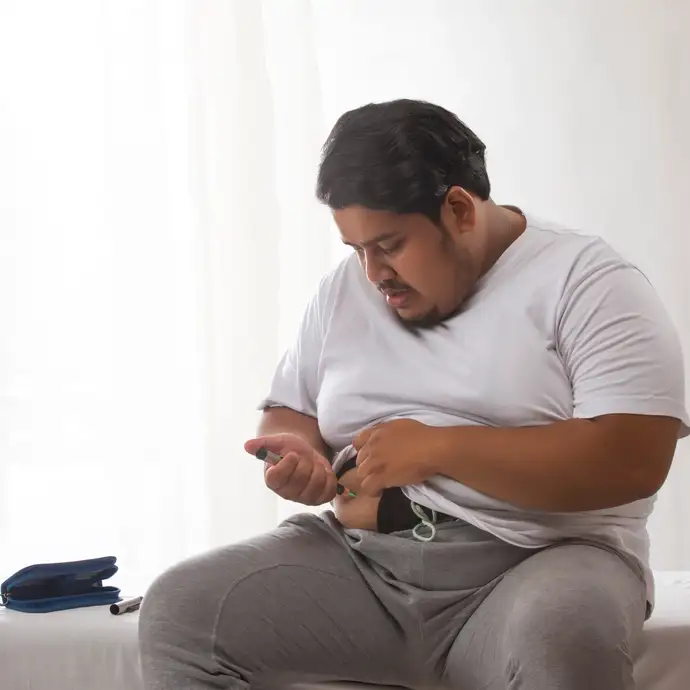 a person is sitting on the edge of a bed, checking their blood sugar levels with a glucose meter