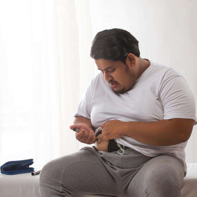 a person is sitting on the edge of a bed, checking their blood sugar levels with a glucose meter