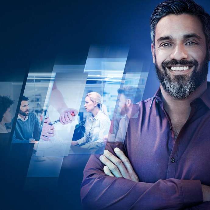 Homem barbudo com braços cruzados sorrindo em frente a imagens de profissionais em uma reunião