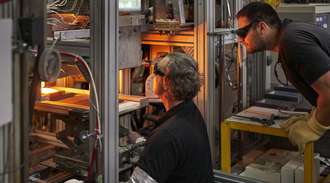 Two SCHOTT employees look through protective goggles at molten glass on a production machine.