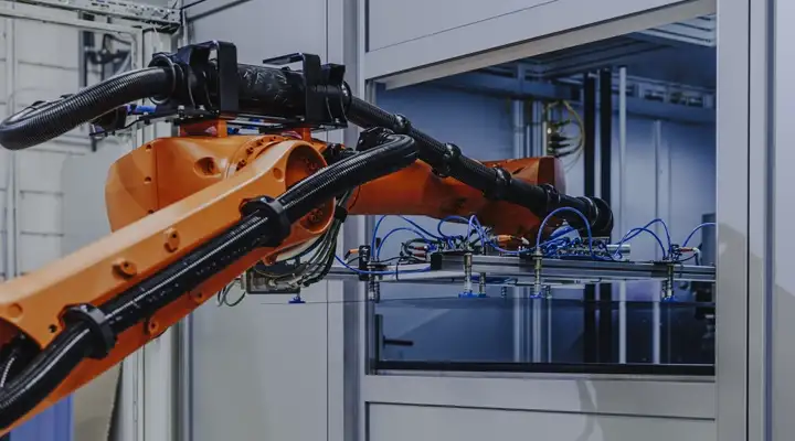 A robotic arm in an industrial setting operating near a machine enclosure.