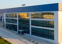 Modern industrial building with blue accents, large flat roof, and multiple loading docks, and adjacent warehouses.