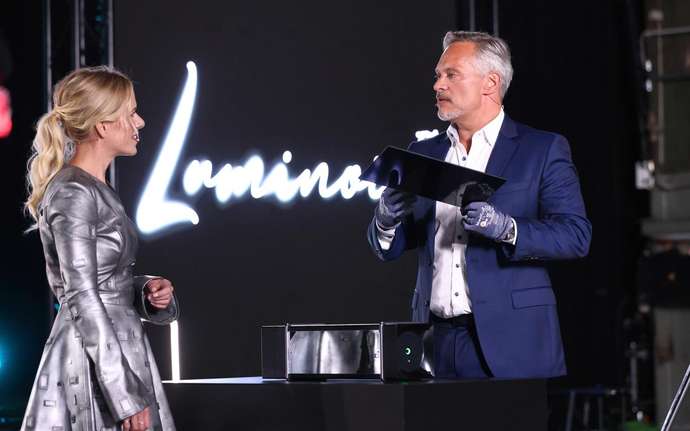 Man and woman on stage with panel of SCHOTT CERAN® Luminoir™ black glass-ceramic cooktop	