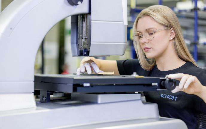 Woman sitting in front of a machine and inspecting a golden microelectronic package