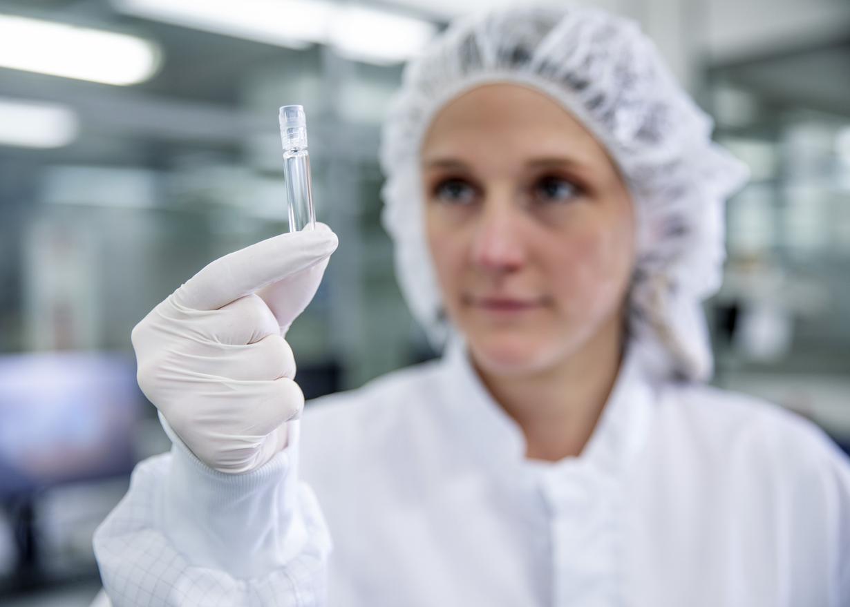 Woman in cleanroom clothing holds up a prefillable glass syringe.