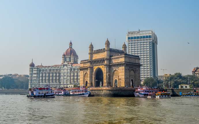 	 Gateway of India in Mumbai, surrounded by boats, with the Taj Mahal Palace Hotel in the background.