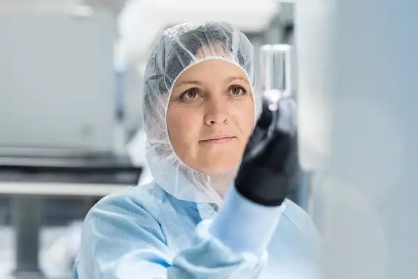 Eine Person in Reinraumbekleidung hält ein zylindrisches Glasbauteil prüfend ins Licht.