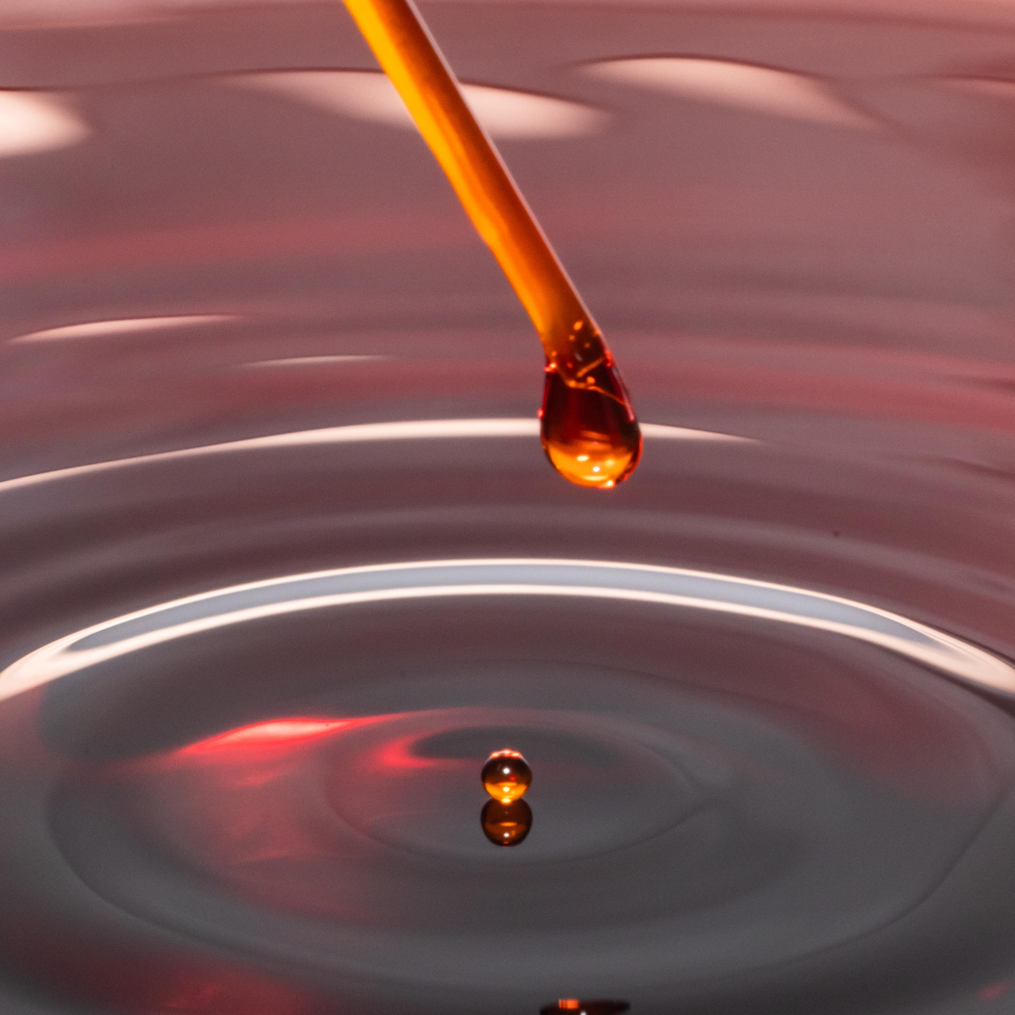 Red droplet from pipette creating waves.