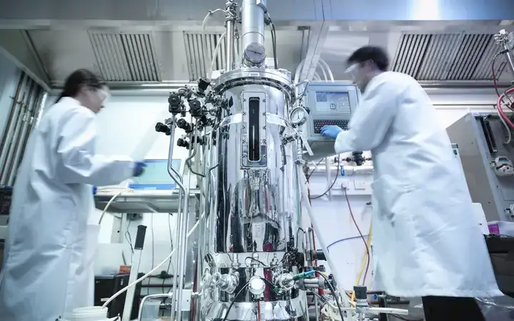 Scientists next to a bioreactor working on protein production in a laboratory