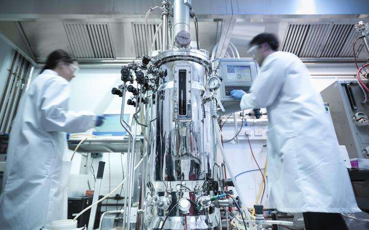 Scientists next to a bioreactor working on protein production in a laboratory
