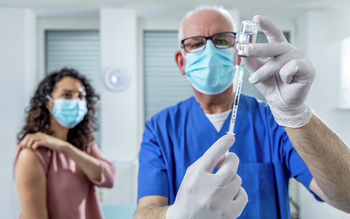Doctor filling a syringe with patient in background