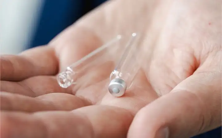 A hand holding two transparent glass cartridges in a close-up view.