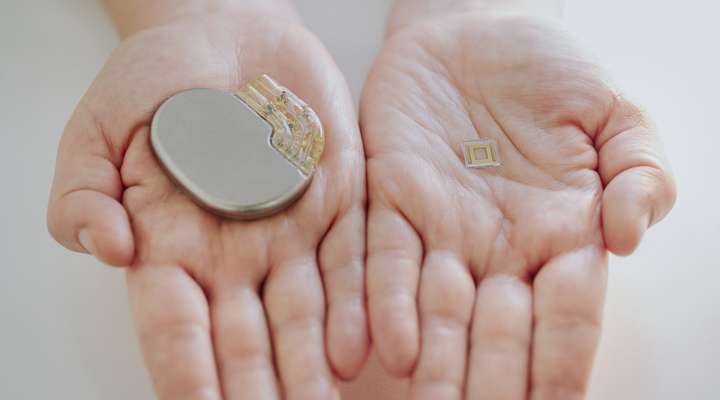 	 A person holding a large implantable medical device and a small implant featuring Primoceler Proteon ™ glass encapsulation, for size comparison.