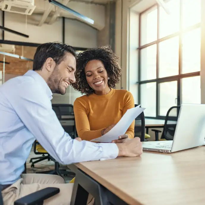 Homens e mulheres sorrindo sobre um laptop enquanto olham para um documento