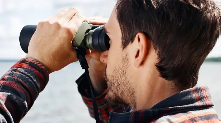 Man looking through binoculars across lake