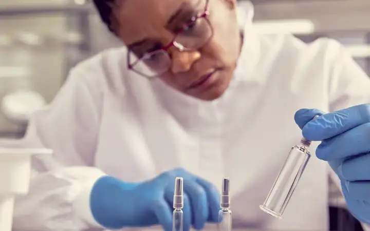 Scientist in gloves and lab coat examining syringe components at a laboratory bench
