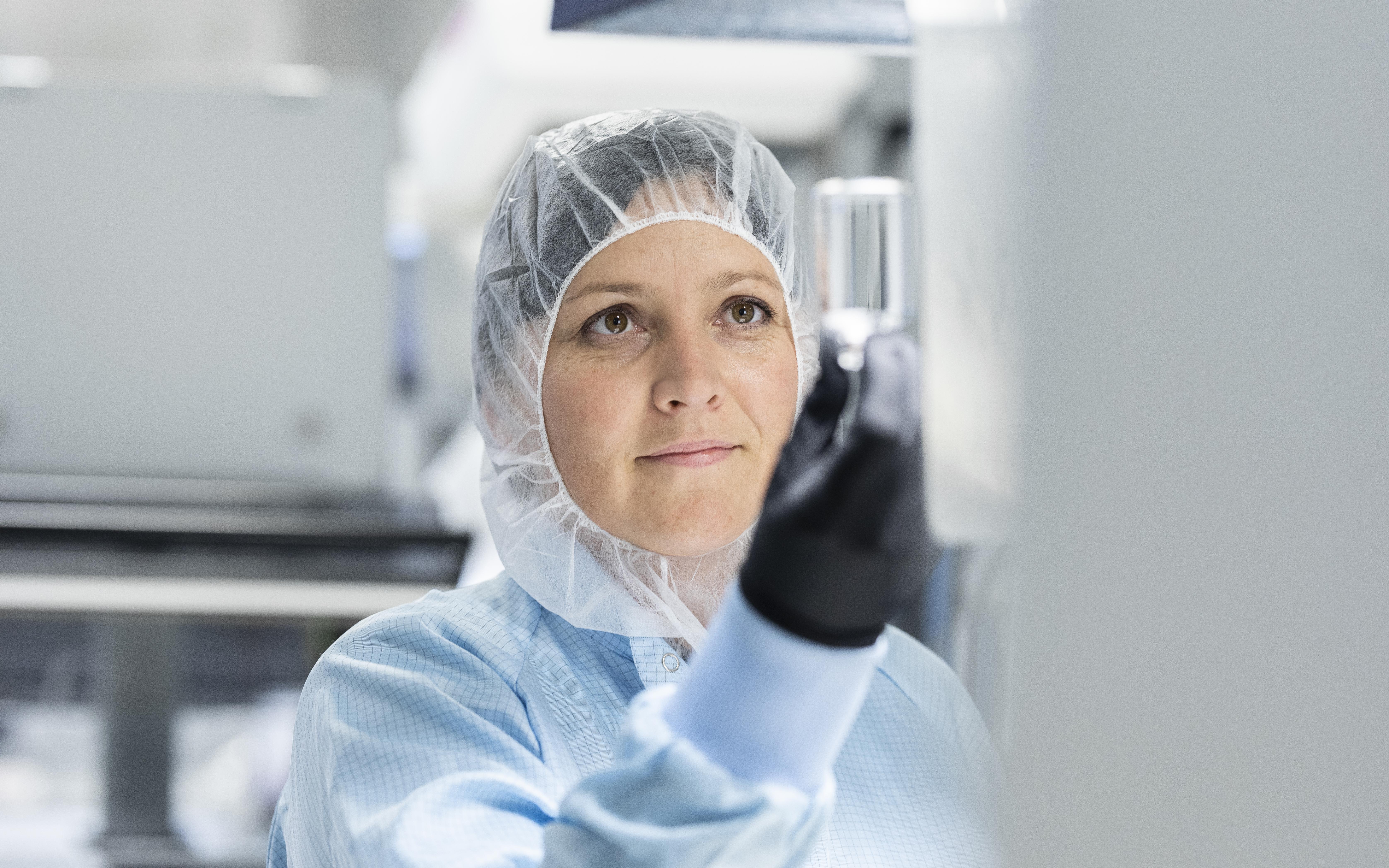 Female scientist inspects a clear glass vial in a laboratory	