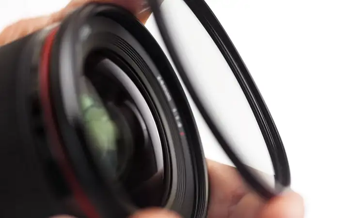 Hand holding a glass optical filter over a camera lens