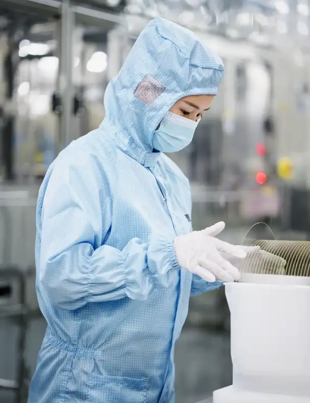 A cleanroom employee wearing protective gear inspects glass wafers.
