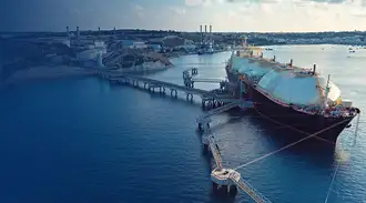 A liquefied natural gas (LNG) ship with large storage tanks on deck is docked at a harbor.