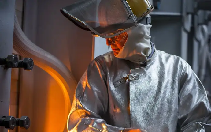 Man in protective suit in front of a melting tank.