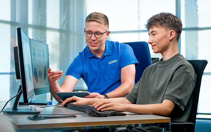 Zwei Personen sitzen vor einem Computerbildschirm und besprechen gemeinsam technische Inhalte.