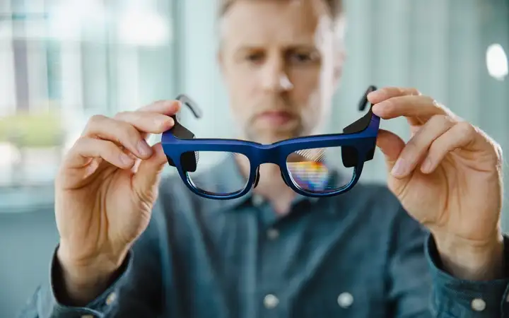 Man holding blue smart glasses with SCHOTT(R) reflective waveguide