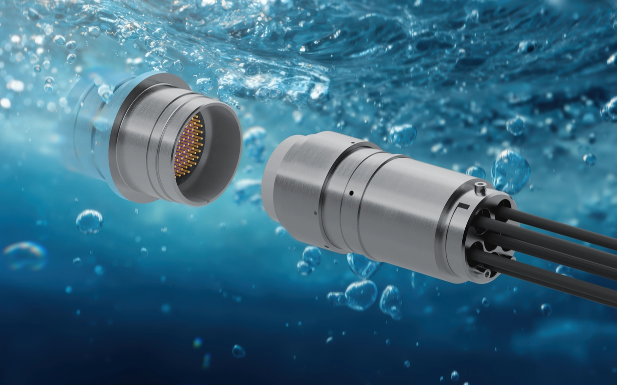 Two metallic connectors submerged in water, one with pins and the other with cables extending from it.