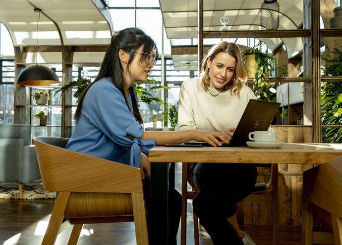 Two women sitting together at a table looking at a laptop