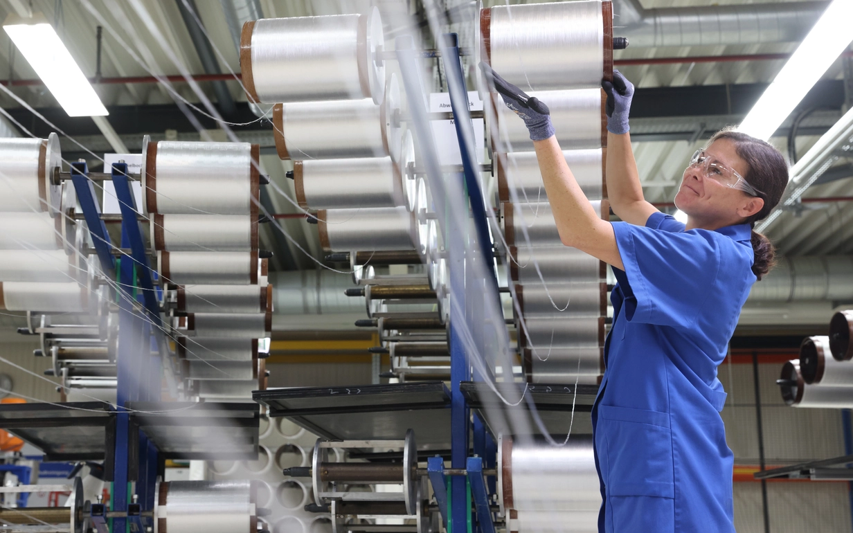 Frau in blauer SCHOTT Arbeitskleidung in der Produktion von faseroptischen Leitern, die auf Rollen aufgewickelt sind.