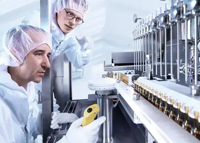Two scientists looking at glass processing equipment producing ampoules