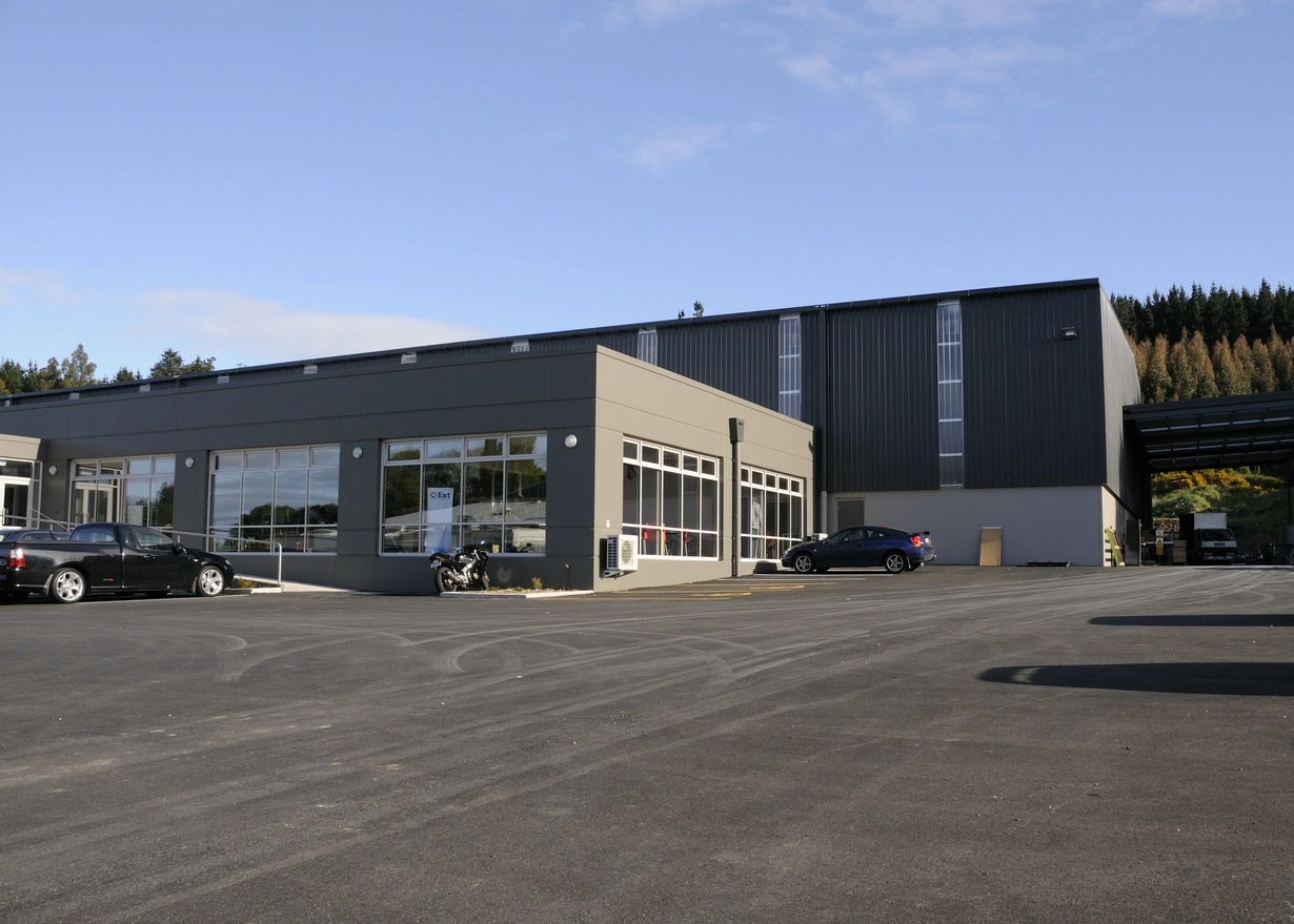 A factory building with a parking lot and cars parked in front