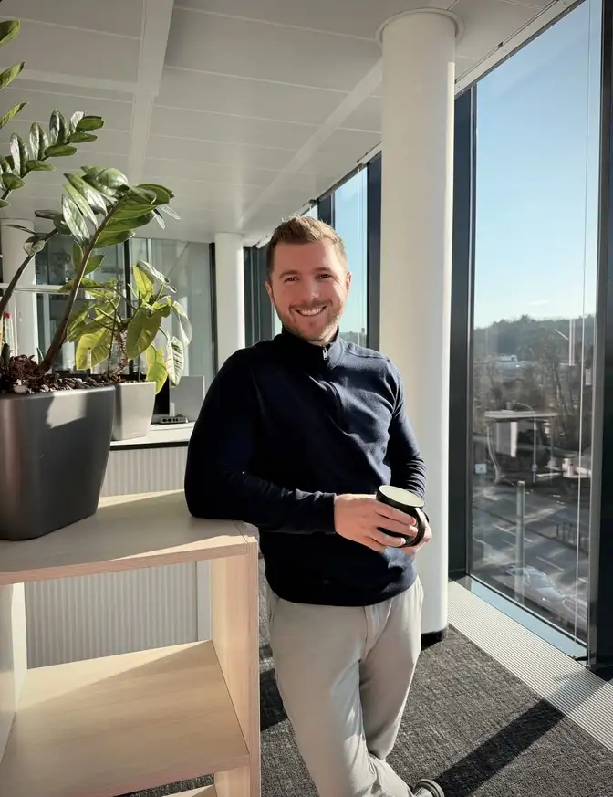 Eine Person in Business‑Kleidung steht mit verschränkten Armen in einem Büro.