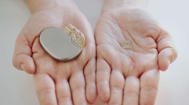 	 A person holding a large implantable medical device and a small implant featuring Primoceler Proteon ™ glass encapsulation, for size comparison.