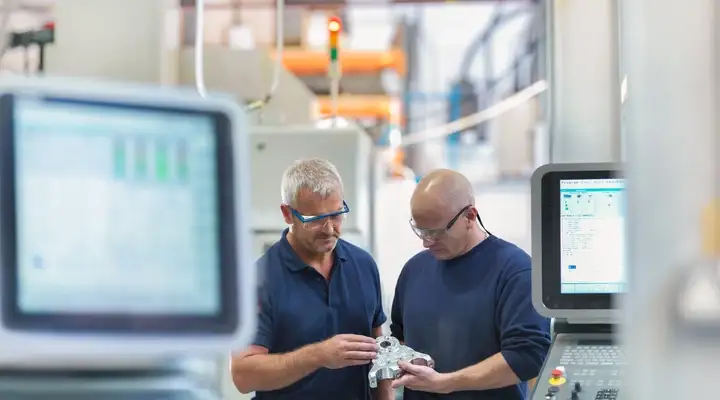 Two engineers inspect a part in front of manufacturing equipment